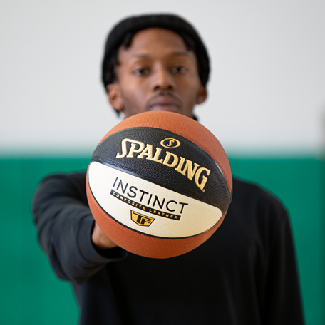 Male Model palming Instinct TF basketball wearing a black Spalding long sleeve tee. 